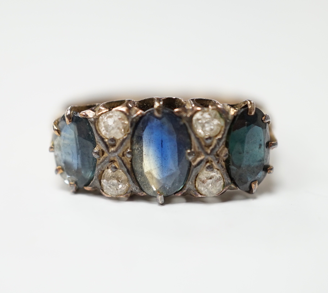 An early 20th century 18ct and graduated three stone sapphire set half hoop ring, with diamond chip spacers, size P, gross weight 3.8 grams.